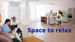 disabled woman reading on sofa and people gathered at desk chatting in open, brightly lit professional recreational space, text reads 'space to relax' - clansman interiors office winter refresh - winter office refurbishment glasgow - office refurbishment scotland